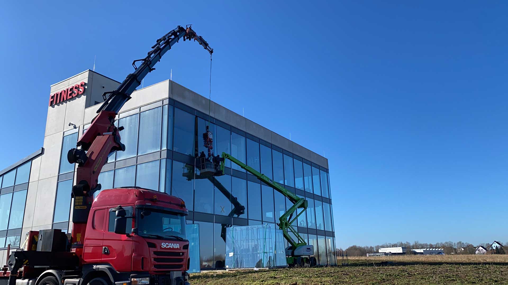 Kran arbeitet an Glasfassade eines Bürogebäudes unter blauem Himmel.
