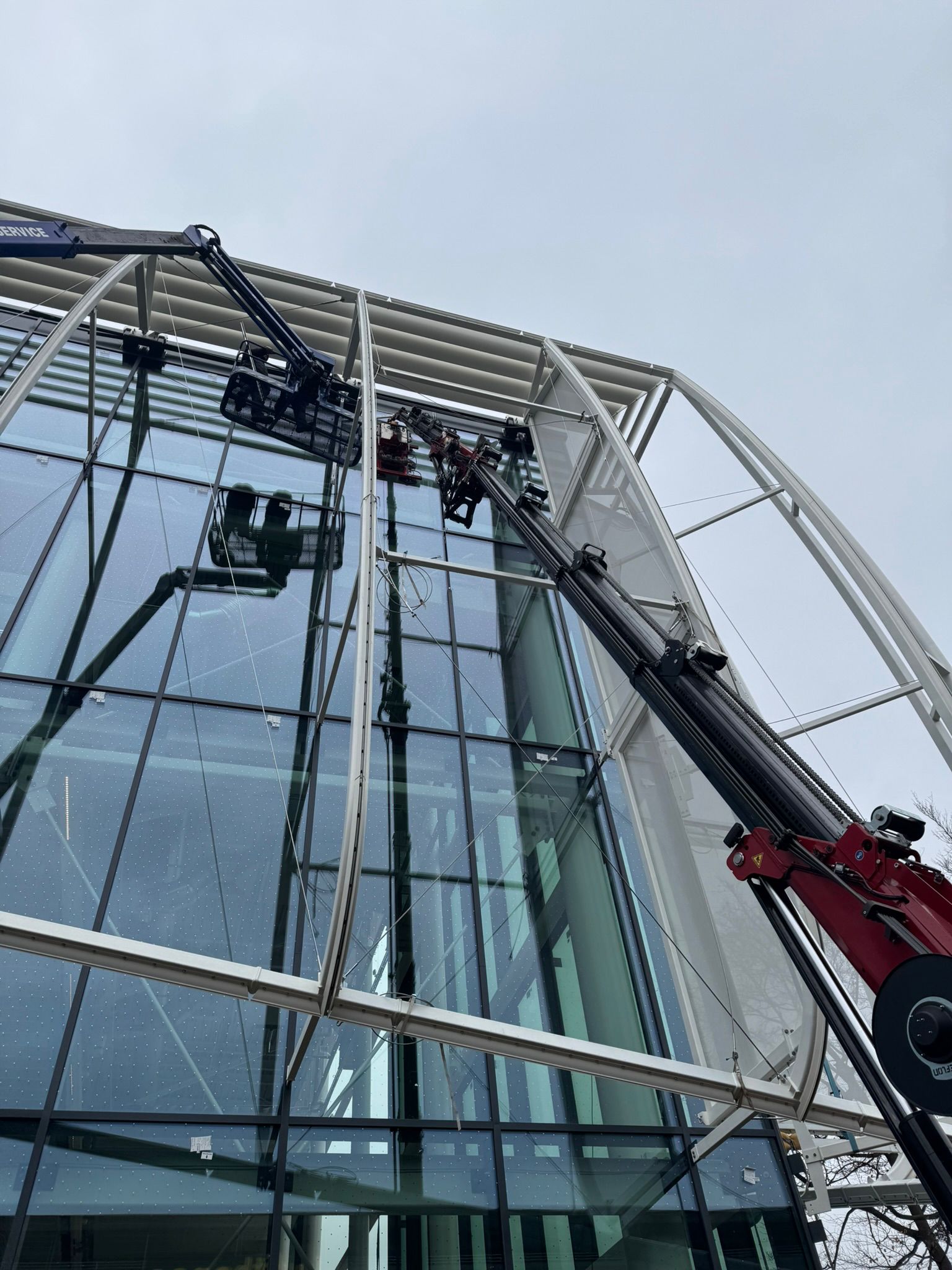 Zwei Krane montieren große Gebäudeelemente an Glasfassade.